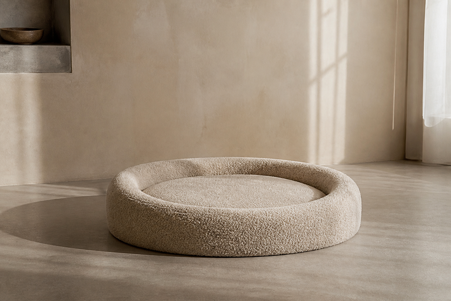 A round oatmeal boucle dog bed on a pale concrete floor